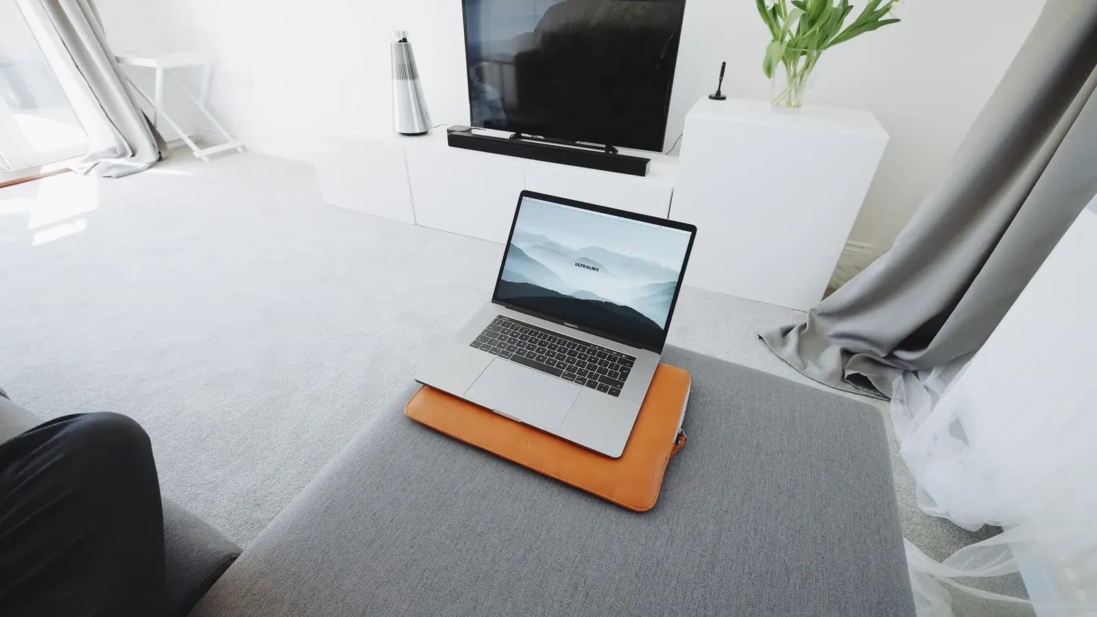 Laptop open on an ottoman in front of a television and soundbar